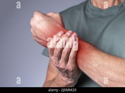 Uomo che soffre di dolore al polso e che tiene una mano dolorosa con punto rosso primo piano. Lesioni alle mani. Assistenza sanitaria, concetto di medicina. Foto di alta qualità Foto Stock