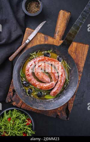 Tradizionale salsiccia italiana fritta salsiccia di carne all'aperto servita con insalata di rucola e olive come vista dall'alto in una padella di ghisa Foto Stock