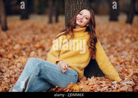Giovane donna modello in autunno parco con foglie di acero giallo fogliame. Moda stagione autunnale. Foto Stock