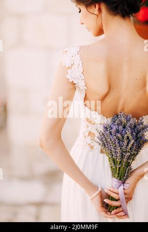 Sibenik, Croazia - 05.06.17: Sposa in un abito in pizzo bianco si alza con la testa inchinato e tiene un bouquet di lavanda legato con un lil Foto Stock