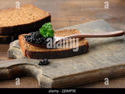 Caviale di paddlefish nero sgranato fresco in cucchiaio di legno marrone su un tavolo marrone Foto Stock