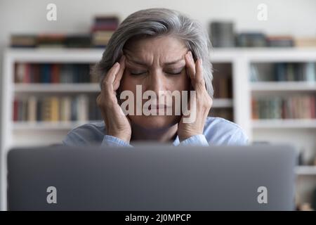 La donna d'affari più anziana tocca i templi soffre di emicrania, primo piano Foto Stock