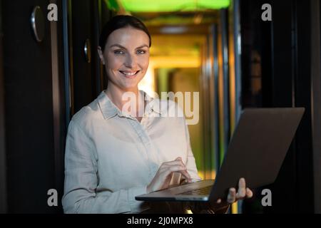 Ritratto di ingegnere caucasico femmina sorridendo mentre si usa il computer portatile in sala server Foto Stock