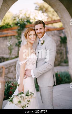 Lo sposo abbraccia con un bouquet vicino all'arco di pietra Foto Stock