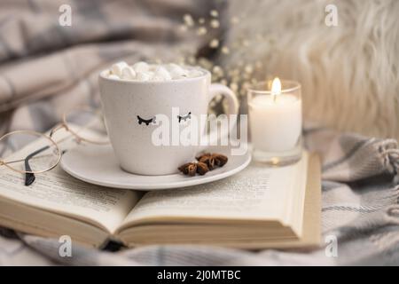 Tazza di cacao caldo con marshmallows su libro con candela Foto Stock