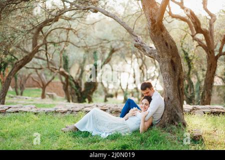 Kotor, Montenegro - 21.06.17: L'uomo seduto abbraccia una donna che giace accanto a lui su erba verde e la bacia sulla corona vicino ad un albero i Foto Stock