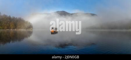 Un motoscafo in legno su un lago tranquillo in una mattinata di nebbia Foto Stock