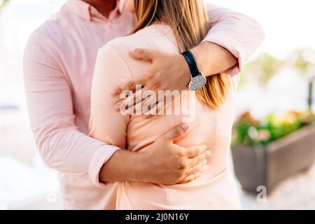 L'uomo in una camicia pastello e un orologio da polso abbraccia una donna in una blusa arancione. Primo piano Foto Stock