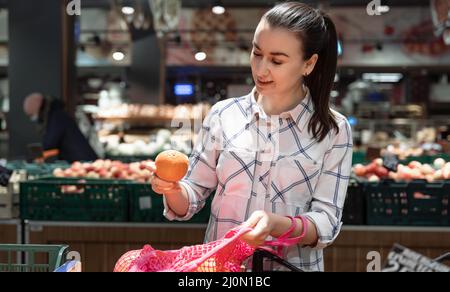 Una giovane donna sceglie la frutta in un supermercato. Foto Stock