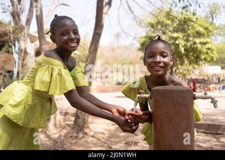 Mani pulite per una vita più sana, belle ragazze africane al punto d'acqua del loro villaggio. Foto Stock