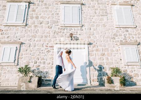 Kotor, Montenegro - 20.06.17: Sposo ha alzato la mano della sposa, camminando lungo la strada passando un vecchio edificio con le persiane sulla vittoria Foto Stock