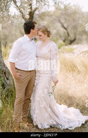 Lo sposo bacia la sposa sulla fronte mentre si alza nell'oliveto Foto Stock