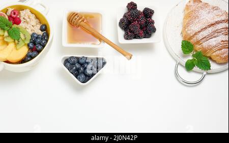 Piatto con farina d'avena e frutta, mezzo succo d'arancia maturo e spremuto di fresco in un decanter trasparente in vetro, miele in una ciotola sopra Foto Stock