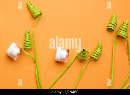 Vasetti vuoti di vetro bianco con coperchio di plastica su sfondo arancione con decorazioni verdi. Confezione per crema, gel, siero, pubblicità e. Foto Stock