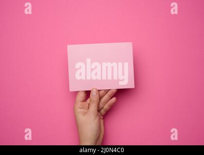 Mano femmina che tiene carta rosa vuota su sfondo rosa. Copia Incolla immagine o testo, primo piano Foto Stock