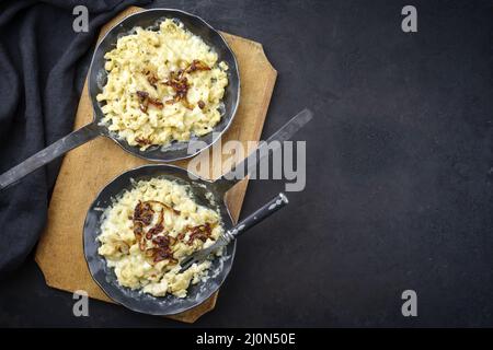 Tradizionale spaetzle di formaggio svevo con cipolle fritte servito come vista dall'alto in una padella in ghisa su una tavola nera rustica con Foto Stock