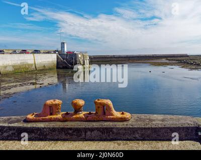 La luce di navigazione e l'ingresso al Porto Seahouses preso dal Quay interno, con una corda Bollard giallo in primo piano. Foto Stock