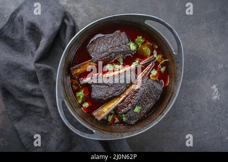 Tradizionali costolette di manzo brasate in salsa di vino rosso servite come vista dall'alto in un moderno forno olandese Foto Stock