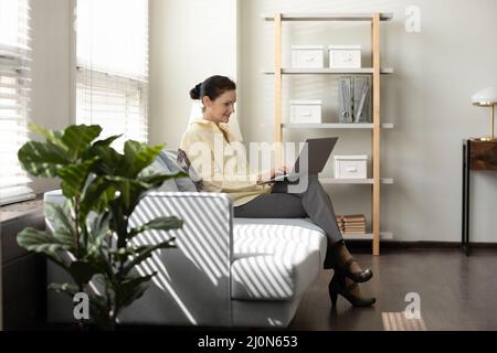 Donna d'affari matura e positiva seduta sul divano in ufficio Foto Stock