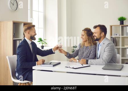 Sorridente agente immobiliare maschile dà le chiavi alla giovane famiglia che insieme acquistare prima casa. Foto Stock