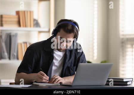 Ragazzo allegro studente in cuffie che si diverse a studiare online al portatile Foto Stock
