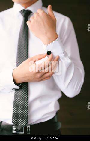 Uomo in cravatta e pantaloni bottoni un cucciolo sulla manica di una camicia bianca Foto Stock