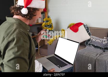 Uomo disabile caucasico a santa Hat utilizzando un computer portatile con spazio copia a casa durante il natale Foto Stock