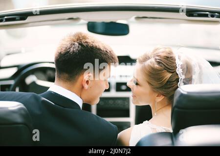 Gli sposi sorridono l'uno all'altro mentre si siedono in un convertibile. Primo piano Foto Stock