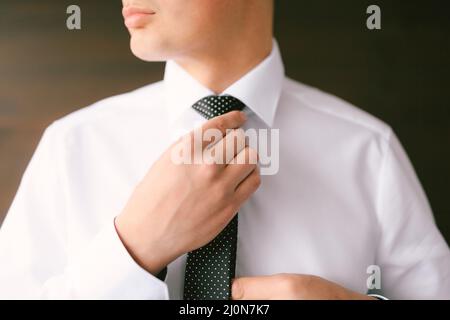 L'uomo in camicia bianca raddrizza il collo e la cravatta Foto Stock