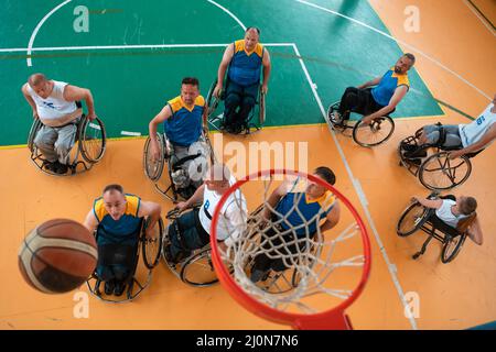 Disabili veterani di guerra o di lavoro squadre miste di pallacanestro e di età in carrozzina che giocano una partita di allenamento in una palestra sportiva. Foto Stock