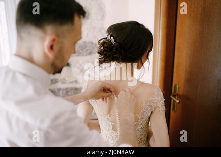 Lo sposo fissa i bottoni sul vestito della sposa. Primo piano Foto Stock