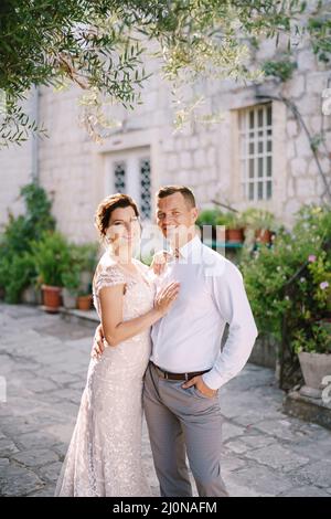 Gli sposi sorridenti si trovano nel cortile di una casa su pietre di pavimentazione Foto Stock