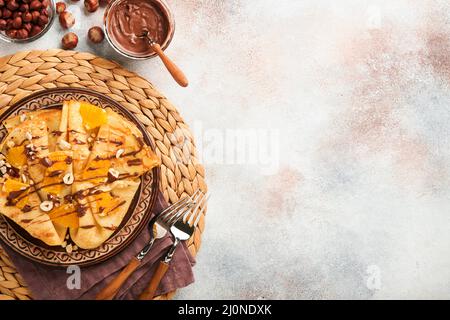 Crepes suzette con arance e cioccolato. Crepes sottile con cioccolato spalmato, nocciole e fette d'arancia frutta in piatto per colazione su cemento vecchio Foto Stock