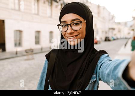 Giovane donna musulmana che indossa hijab sorridendo mentre scatta foto selfie a City Street Foto Stock
