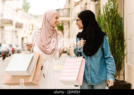 Due giovani donne musulmane sorridenti che camminano su una strada trasportando le borse della spesa Foto Stock