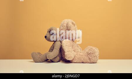 Due graziosi orsacchiotti marroni seduti su sfondo giallo, giocattolo per bambini Foto Stock