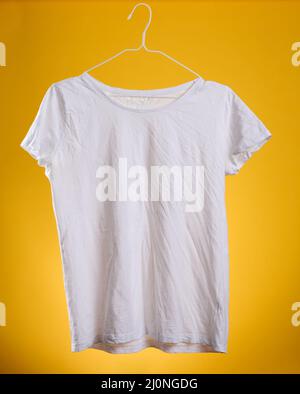 T-shirt in cotone bianco ricalcato appesa a un appendiabiti su sfondo giallo, abiti estivi Foto Stock