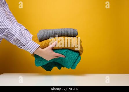 Donna che tiene una pila di maglioni piegati a maglia su uno sfondo giallo. Lavare i vestiti, pulire le cose Foto Stock