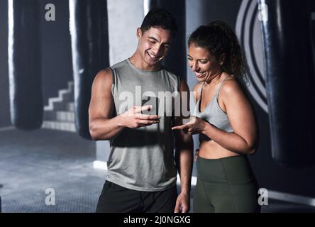 Questa è un'ottima app con cui tenere traccia dei nostri progressi. Shot di due persone sportive che guardano qualcosa su un cellulare insieme in una palestra. Foto Stock