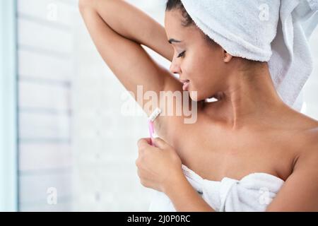 Una rasatura davvero profonda. Scatto di una giovane donna attraente che rasa le sue ascelle con un rasoio nel bagno. Foto Stock