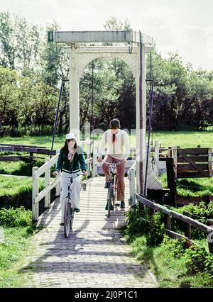 Vintage Netherlands 1970s, coppia di turisti di mezza età in bicicletta, ponte levatoio bianco, Marken, Waterland, Olanda settentrionale, Paesi Bassi, Europa, Foto Stock