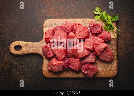 Cubetti di carne cruda di manzo per stufato su tagliere di legno Foto Stock