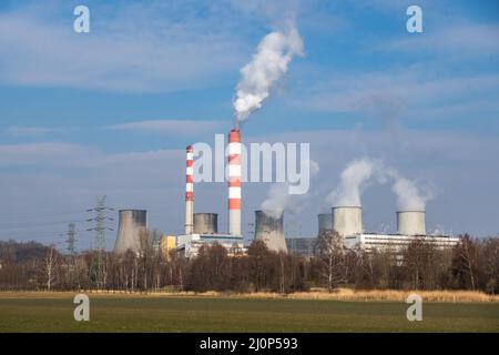 Vista distante di una centrale elettrica alimentata a carbone. Fumando camini e vapore dalle torri di raffreddamento. Foto scattata in una giornata di sole, illuminazione a contrasto. Foto Stock