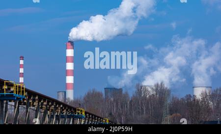 Vista distante di una centrale elettrica alimentata a carbone. Fumando camini e vapore dalle torri di raffreddamento. Foto scattata in una giornata di sole, illuminazione a contrasto. Foto Stock