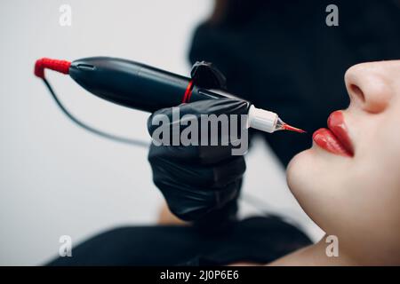 Cosmetologist applying red permanent make up tattoo on young woman lips Stock Photo