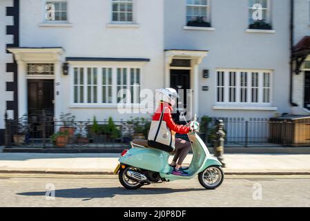 Donna elegante che guida uno scooter classico a motore attraverso una strada a Kensington, Londra, Regno Unito. Vespa Primavera 125 pilota Foto Stock