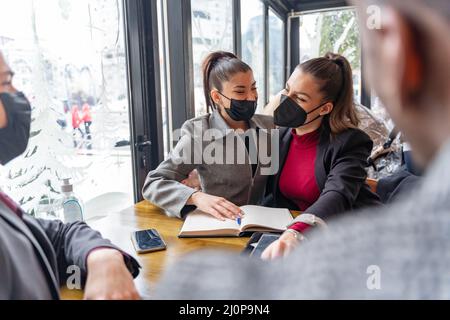 Due donne di affari stupefacenti ed attraenti sono hugging e sorridenti, maschere covid Foto Stock