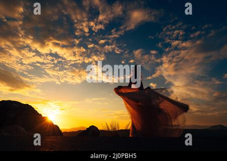 Sposati in un abito scintillante si erge su una montagna sullo sfondo di un cielo al tramonto Foto Stock