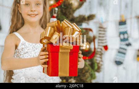 Bella ragazza di 8 anni in un abito bianco principessa contiene una scatola regalo rossa con un nastro d'oro e un grande aratro a nastro su di esso. Natale Foto Stock