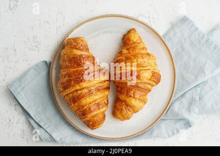 Due deliziosi croissant su piatto e bevanda calda in tazza. Colazione francese al mattino Foto Stock